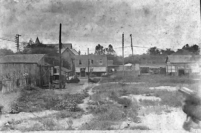 Unknown town with dirt roads, a blacksmith shop, buildings, and a buggy behind a building.
